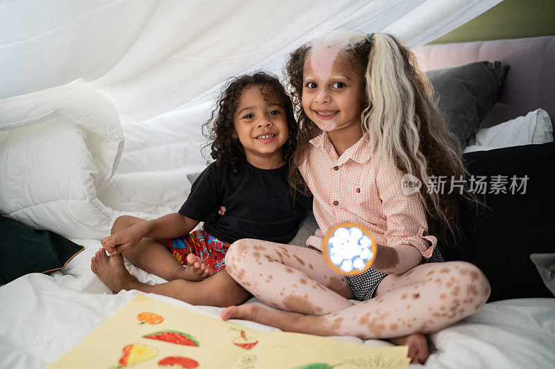 Portrait of siblings in a blanket tent at home - girl with piebaldism